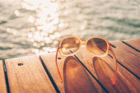 Sunglasses at the wooden pier during sunset. Luxury vacation resort. Holiday getaway concept. Horizontal, warm toningの写真素材