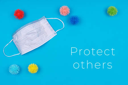 Medicine mask with plastic balls viruses on the blue background with Protect others wording. Epidemic, seasonal viruses, social isolation, coronavirus COVID-19 concept. Place for textの写真素材