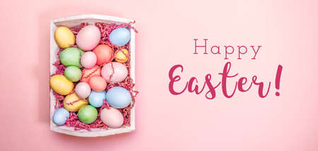 Multicolor eggs in a white tray. Creative Easter concept. Modern solid pink background. Horizontal, wide screen banner. Living coral accent, color of the year 2019の写真素材