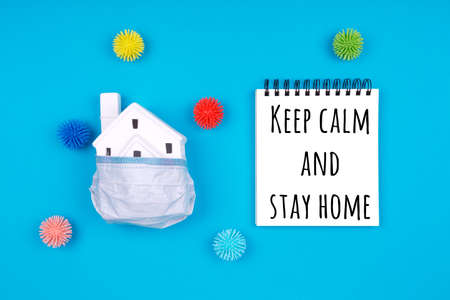 Cute little house covered with medicine mask and plastic balls aka viruses on the blue with Keep calm and stay home wording. Epidemic, social isolation, coronavirus COVID-19 concept. Option with textの写真素材