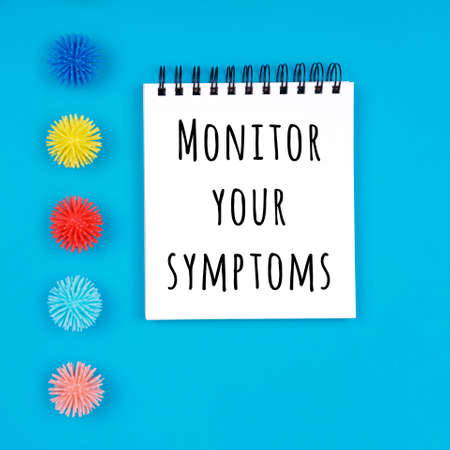 Paper notebook with plastic balls viruses on the blue background with Monitor your symptoms wording. Epidemic, social isolation, coronavirus COVID-19 concept. Square formatの写真素材