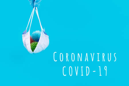 Hand in latex glove holds disposable mask with plastic balls aka viruses on the blue with Coronavirus COVID-19 wording. Epidemic, social isolation, coronavirus COVID-19 concept. Option with textの写真素材