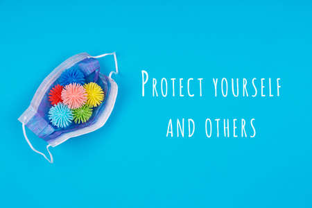 Medicine mask with plastic balls as germs on the blue with Protect yourself and others wording. Epidemic, social isolation, coronavirus COVID-19 concept. Oprion with text, easy cut to bannerの写真素材