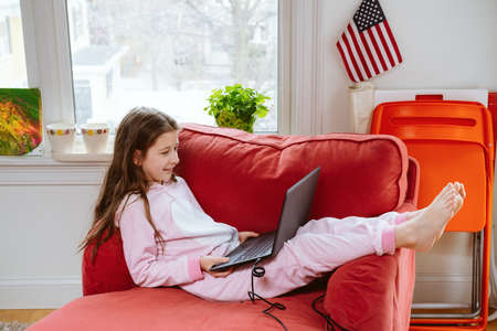 Preteen girl enjoyes homeschooling in comfy pijama and cozy sofa chair. Remote education, virus protection, social distancing and lockdown concept. household items at the backの写真素材