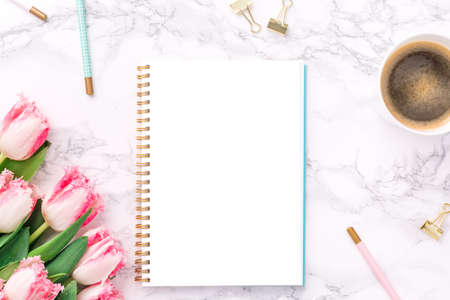 Pink tulips with festive stationary and coffee on white marble background. Feminine job, gender equality, home office and career concept. Isolated white copy space on the paper. Top view. Horizontalの写真素材