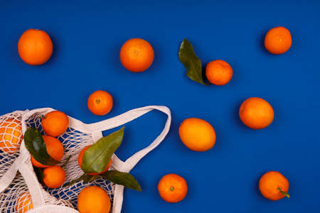 Mesh cotton reusable bag with mandarines on classic blue. Eco friendly shopping, ecology and healthy...