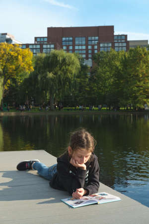 Girl enjoyes reading by the pond. Relaxation and self education concept