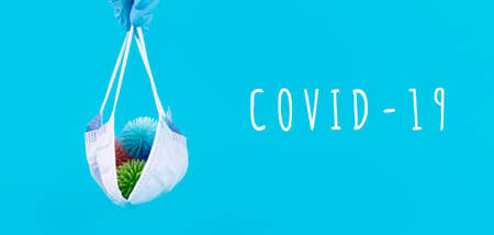 Hand in latex glove holds disposable mask with plastic balls as viruses on blue with Coronavirus COVID-19 wording. Epidemic, social isolation, coronavirus COVID-19 concept. Option with text, bannerの写真素材