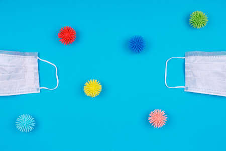 Two medical masks with plastic balls as germs and viruses on the blue background. Epidemic, social isolation, coronavirus COVID-19 concept. With place for textの写真素材