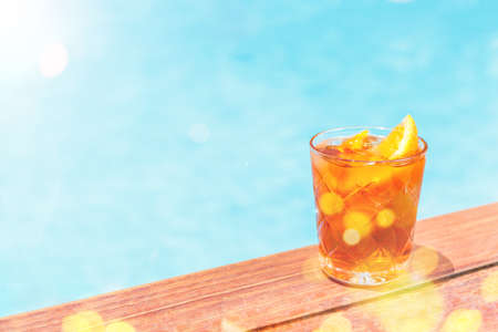 Negroni cocktail near a pool at resort bar or suite patio. Luxury resort, vacation, holiday, getaway, summer time, room service concept. Horizontal with place for text with festive bokeh and sunlightの写真素材