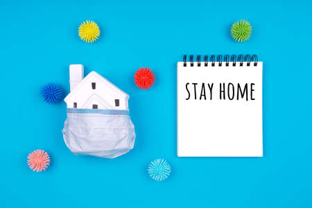 Cute little house covered with medicine mask and plastic balls as viruses on blue with Stay home wording. Epidemic, social isolation, coronavirus COVID-19 concept. Option with textの写真素材