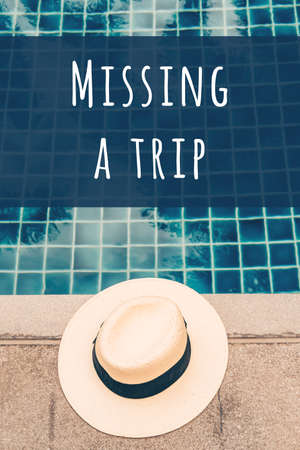 Straw hat at the pool edge with palm reflections in the water with Missing a trip wording. Vacation...