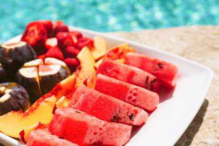 Exotic tropical fruit plate on the pool edge. Healthy treat, luxury resort vacation conceptの写真素材