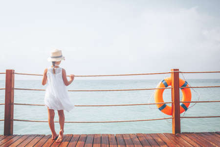 Suntanned girl in white dress enjoyes sea view at the wooden pier. Vacation, get away, travel concept. Toned image, place for textの写真素材