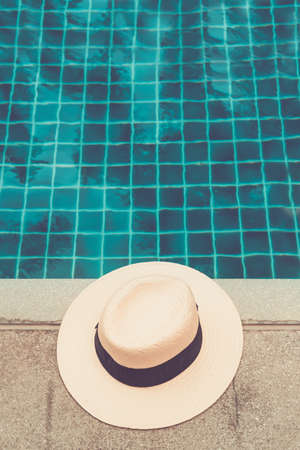 Straw hat at the pool edge with palm reflections in the water. Relax vacation, sun protection, travel fashion conceptの写真素材