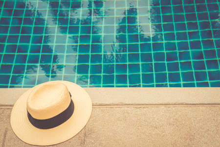 Straw hat at the pool edge with palm reflections in the water. Relax vacation, sun protection, travel fashion concept. Place for text, toned imageの写真素材