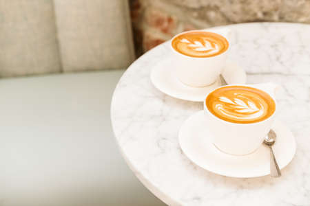 Cups of cappuccino on the white marble table in a modern cafe. Time out, coffee, luxury living, friends meeting concept. Place for textの写真素材