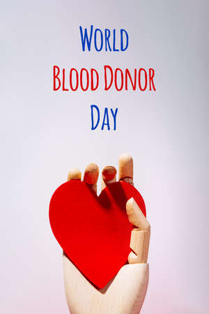 Wooden hand with big red heart in a giving gesture. World Blood Donor Day wording. Donation, help, health issues, antibody plazma concepts.の写真素材