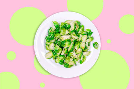 Plate with lightly fried brussels sprouts on the creative futuristic neon green and pink color drop with rounds. Easy cooking at home, healthy eating, vegetarian and vegan concepts in trendy styleの写真素材