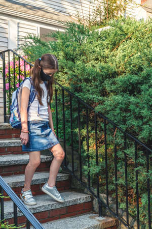 Elementary school student in a cloth dust mask with backpack in the street. Preteen girl is going to...
