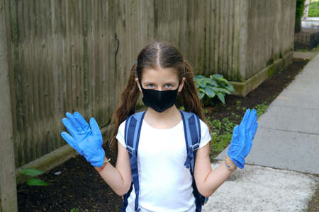 Elementary school student in a cloth dust mask and latex gloves with backpack in the street. Preteen girl is going to school in new normal. Online and hybrid education, back to school conceptの写真素材