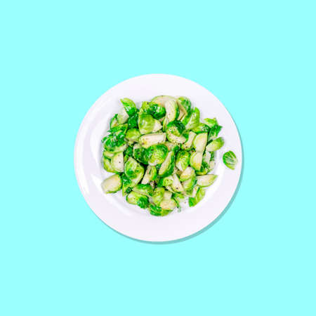 Lightly fried brussels sprouts on a white plate on the solid turquise drop. Easy cooking, healthy eating, cooking at home, vegetarian and vegan concepts. Square social media formatの写真素材
