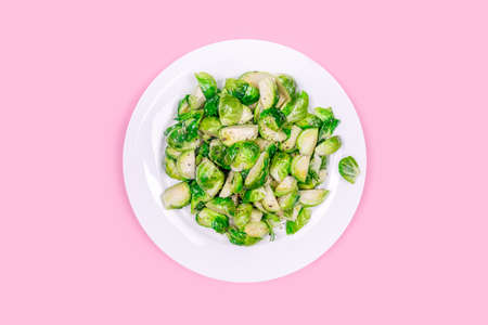 Lightly fried brussels sprouts on a white plate on the solid pink color drop. Easy cooking, healthy eating, cooking at home, vegetarian and vegan conceptsの写真素材
