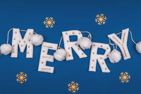 White and golden knitted garland with word MERRY and white pompons on classic blue decorated with golden snowflakes. Holiday celebration concept, Christmas cardの写真素材