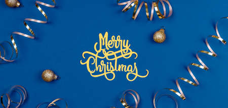 Holiday background with Merry Christmas wording, golden balls, and ribbons on classic blue. Holiday celebration card concept in banner formatの写真素材