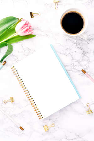Pink tulips with festive stationary and coffee on white marble background. Online and remote work and learning, home office and career concept. Copy space. Top view.. Verticalの写真素材