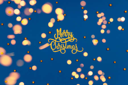 Pattern with golden Merry Christmas wording and holiday round sprinkles on classic blue with festive warm bokeh. Festive holiday drop with place for textの写真素材