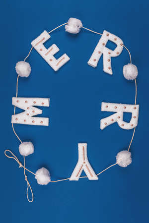 White and golden knitted garland with word MERRY and white pompons on classic blue. Holiday celebration concept, Christmas card. Verticalの写真素材
