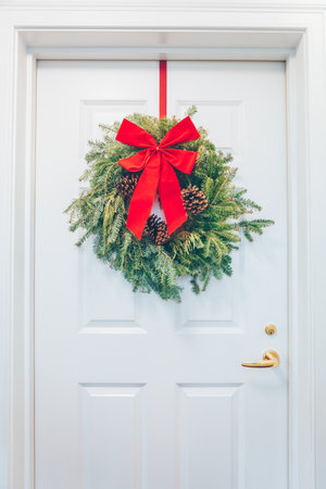 White appartment door with seasonal greens and red bow. Holiday decorations conceptの写真素材