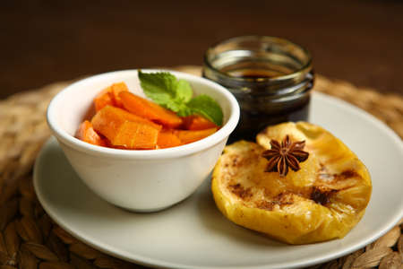 On the plate is a baked pumpkin, an apple and a glass jar with honey, near anise, mint. Wicker substrate and wooden table, composition. Close-upの写真素材