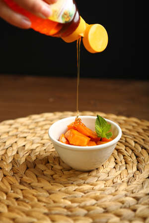 On the plate is a baked pumpkin, near mint. Wicker substrate and wooden table, composition on a black background. Honey movement, action, addition meadの写真素材