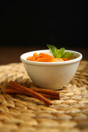 On the plate is a baked pumpkin, near cinnamon, mint. Wicker substrate and wooden table, composition on a black background.の写真素材
