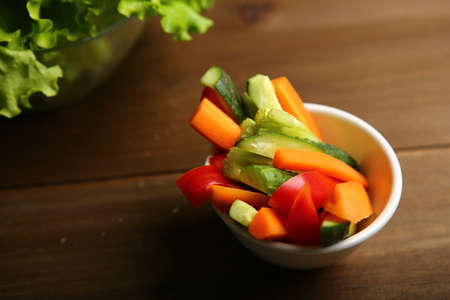 Pepper, carrots, celery, raw cucumber are cut into strips. On the plate. Next to it are lettuce leaves, basil. On a background of cloth, burlap, wooden table, black background.の写真素材