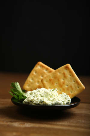 On a dark plate a portion of cottage cheese with greens is decorated with parsley. Low-calorie cookies. Wooden table, dark background. One light source. A healthy diet for those who control their bodyの写真素材