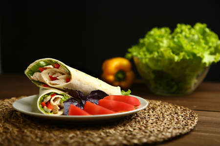 Shaurma without sauce with chicken, pepper, lettuce. Low-calorie roll from pita bread, next to purple basil and slices of tomatoes. Without roasting, raw. In the background pepper and lettuce leavesの写真素材