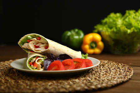 Shaurma without sauce with chicken, pepper, lettuce. Low-calorie roll from pita bread, next to purple basil and slices of tomatoes. Without roasting, raw. In the background pepper and lettuce leavesの写真素材