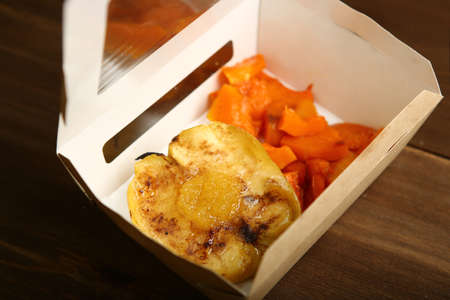 Delivery of dessert from the baked pumpkin and apple in a paper container. A quick snack outside the house. Low-calorie dessert, a healthy diet for those who watch their weight and count caloriesの写真素材