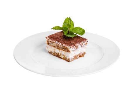 Rectangular piece of Tiramisu with a sprig of mint on a white plate. isolated on white background. Dessert for a menu in a cafe, restaurant, coffee shop side viewの写真素材