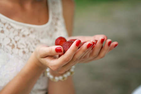 Female hands hold a handful of red strawberries without leaves. Picking berries in the summer,...