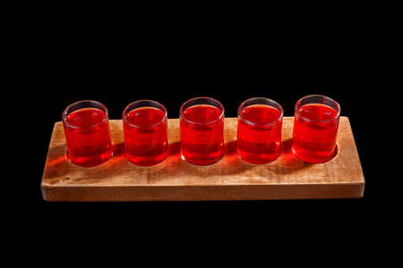 Red, same color transparent cocktails, a set of shots in one row, five servings on a wooden stand,...
