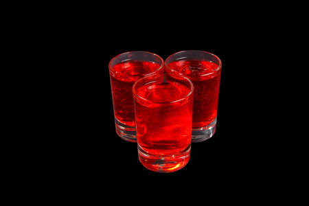 Red transparent cocktails, a set of shots pile, wedge, three servings, with taste of berries, cherries, Side view from above Isolated black backgroundの写真素材