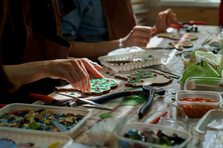 The artist maker mosaic in a wooden harvesting. Two female hands closeup collect mosaic of colored...