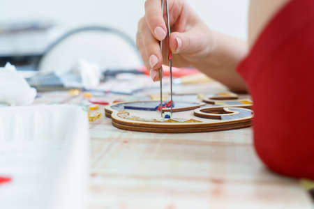 The artist maker mosaic in a wooden harvesting. Female hands closeup collect mosaic of colored...