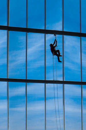 Industrial climber hangs from ropes inside shopping center or exhibition hall building against the blue sky, plenty of free space to signの写真素材