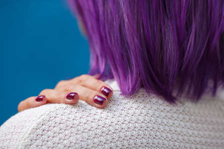 a girl with purple hair stands back, close-up of a womans hand with a beautiful purple manicure, a white knitted jacket, blue background, fingersの写真素材