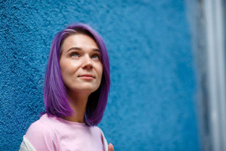 Young lady with bright violet hair grey eyes and pierced nose, in pink t-short, hair coloring,...